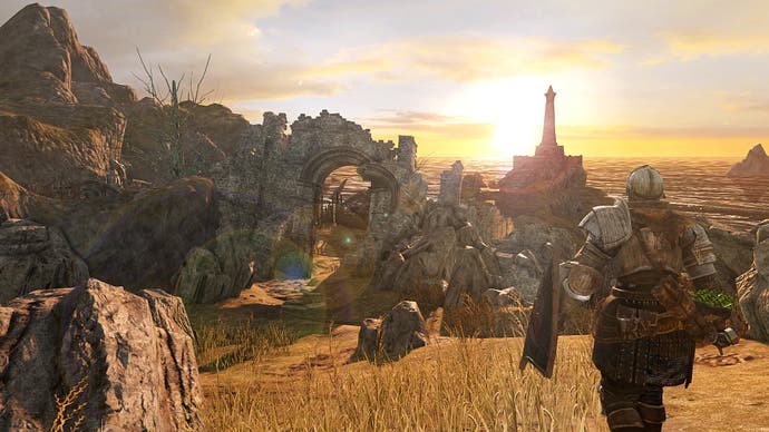 Eine Sonnenuntergangsszene in Dark Souls 2, in der der Spielercharakter in einer Rüstung hinter hoch aufragenden Felsen auf den Horizont blickt.