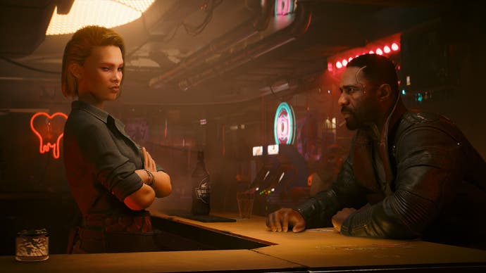 Der offizielle Screenshot von Cyberpunk Phantom Liberty zeigt Idris Elbas Charakter, der in einem dunstigen braunen Raum einer Bar gegenüber sitzt und die Barkeeperin anschaut.